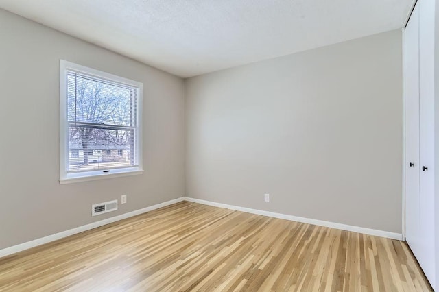 empty room featuring visible vents, light wood-style flooring, and baseboards