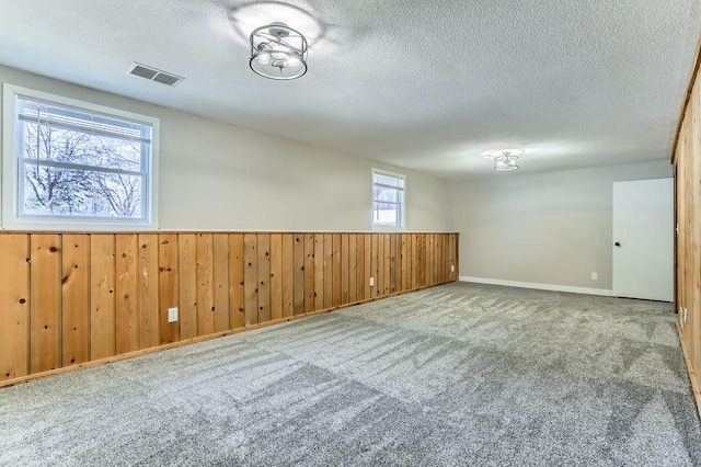 spare room with visible vents, a textured ceiling, wooden walls, wainscoting, and carpet flooring