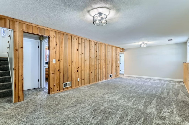 empty room featuring visible vents, a textured ceiling, wooden walls, carpet flooring, and stairs