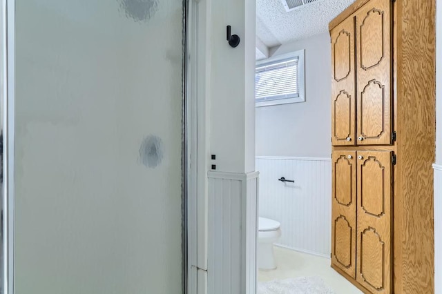 bathroom with wainscoting, a textured ceiling, a shower stall, and toilet