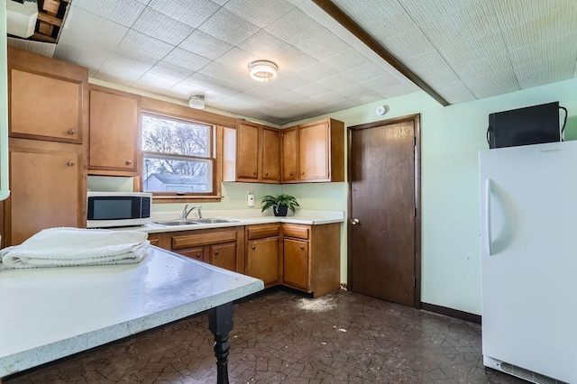 kitchen featuring a sink, freestanding refrigerator, brown cabinetry, light countertops, and baseboards