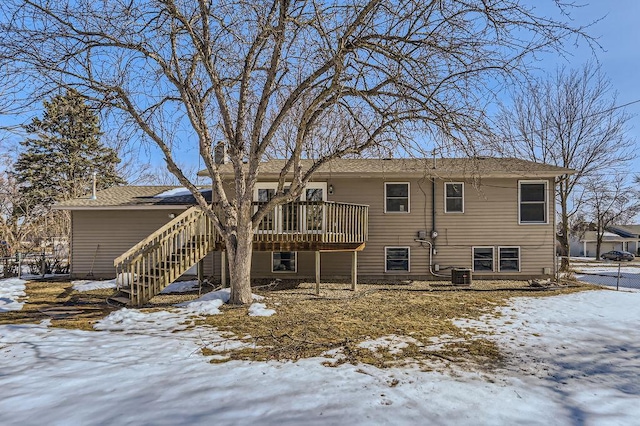 snow covered back of property with stairs, central AC unit, and a wooden deck