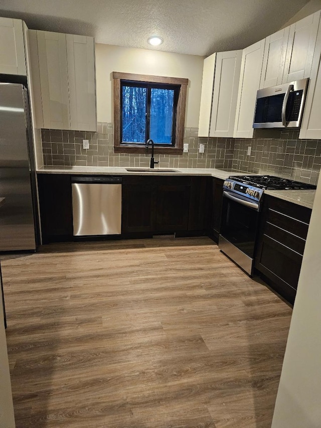 kitchen with stainless steel appliances, sink, light hardwood / wood-style flooring, and white cabinets