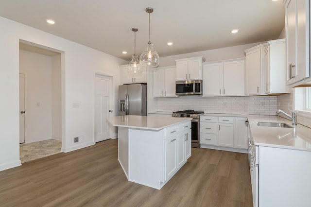 kitchen with appliances with stainless steel finishes, decorative light fixtures, sink, white cabinets, and a center island