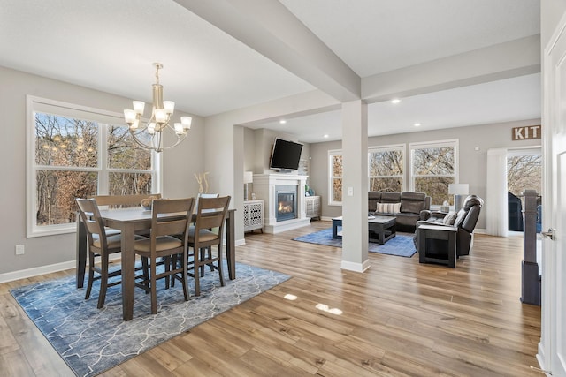 dining room featuring baseboards, a chandelier, light wood-style flooring, recessed lighting, and a glass covered fireplace