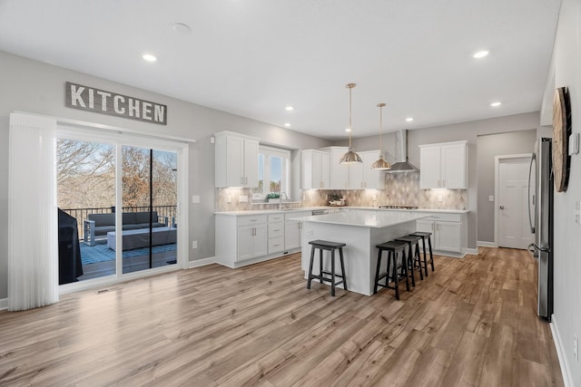 kitchen with a center island, freestanding refrigerator, a breakfast bar area, wall chimney exhaust hood, and decorative backsplash