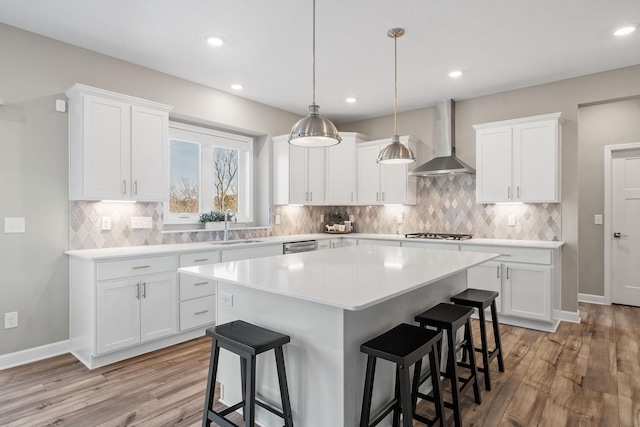 kitchen with light countertops, a breakfast bar area, wall chimney exhaust hood, and a kitchen island