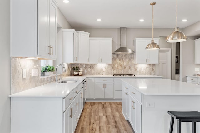 kitchen with light countertops, wall chimney range hood, stainless steel gas stovetop, and a sink