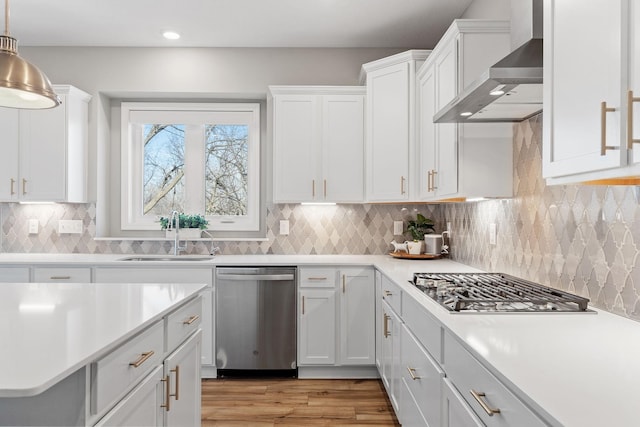 kitchen featuring appliances with stainless steel finishes, wall chimney exhaust hood, white cabinets, and light countertops