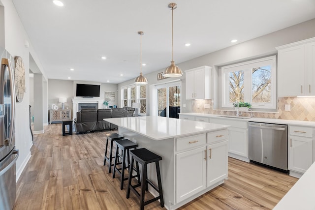 kitchen featuring a sink, backsplash, stainless steel dishwasher, a center island, and light wood finished floors