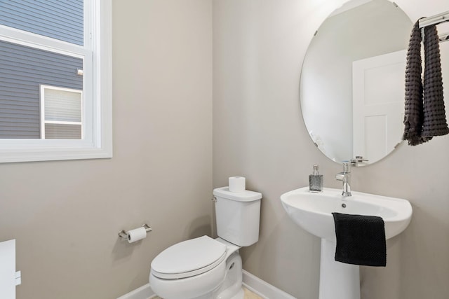 half bath with toilet, baseboards, and a sink