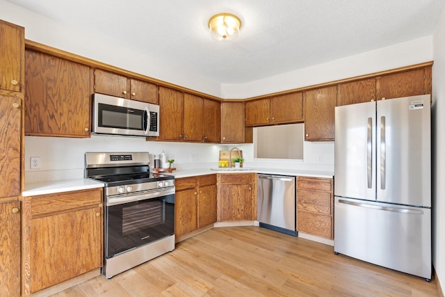 10 94th Cir NW Unit 201, Coon Rapids, MN 55448 - kitchen with appliances with stainless steel finishes, brown cabinets, light countertops, a sink, and light wood-style floors