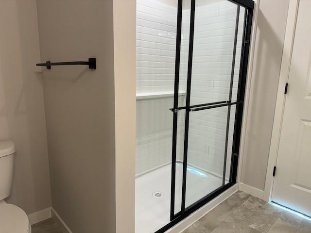 bathroom featuring a shower with door and toilet