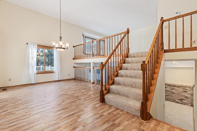 stairs with a high ceiling, hardwood / wood-style floors, and an inviting chandelier