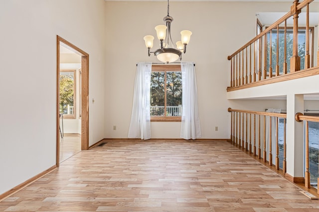 interior space with an inviting chandelier, light hardwood / wood-style flooring, a high ceiling, and plenty of natural light