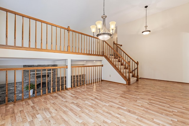 unfurnished living room with an inviting chandelier, high vaulted ceiling, and light wood-type flooring