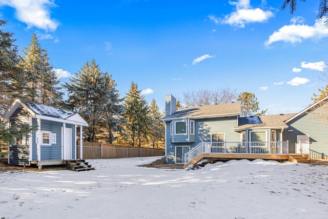 snow covered house featuring a wooden deck and an outdoor structure