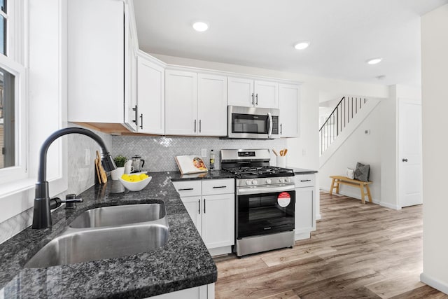 kitchen featuring sink, light hardwood / wood-style flooring, white cabinetry, stainless steel appliances, and dark stone counters