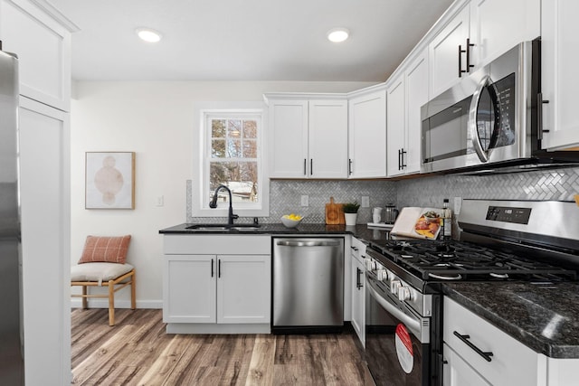 kitchen with sink, white cabinetry, tasteful backsplash, dark stone counters, and stainless steel appliances