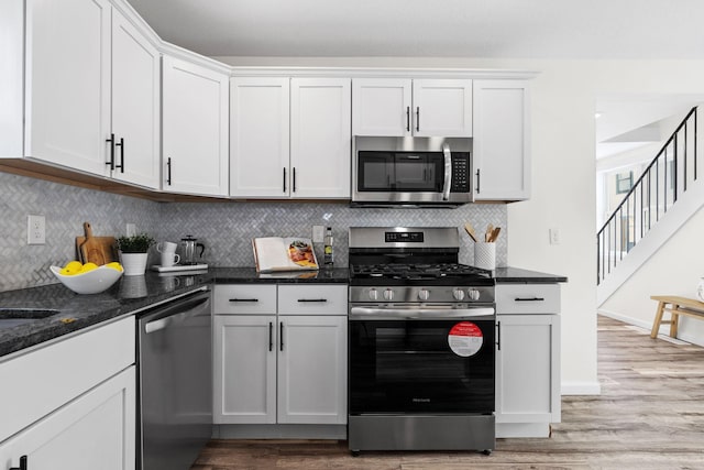 kitchen with white cabinetry, stainless steel appliances, light hardwood / wood-style floors, and dark stone counters