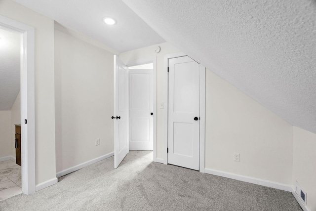 additional living space with light carpet, vaulted ceiling, and a textured ceiling