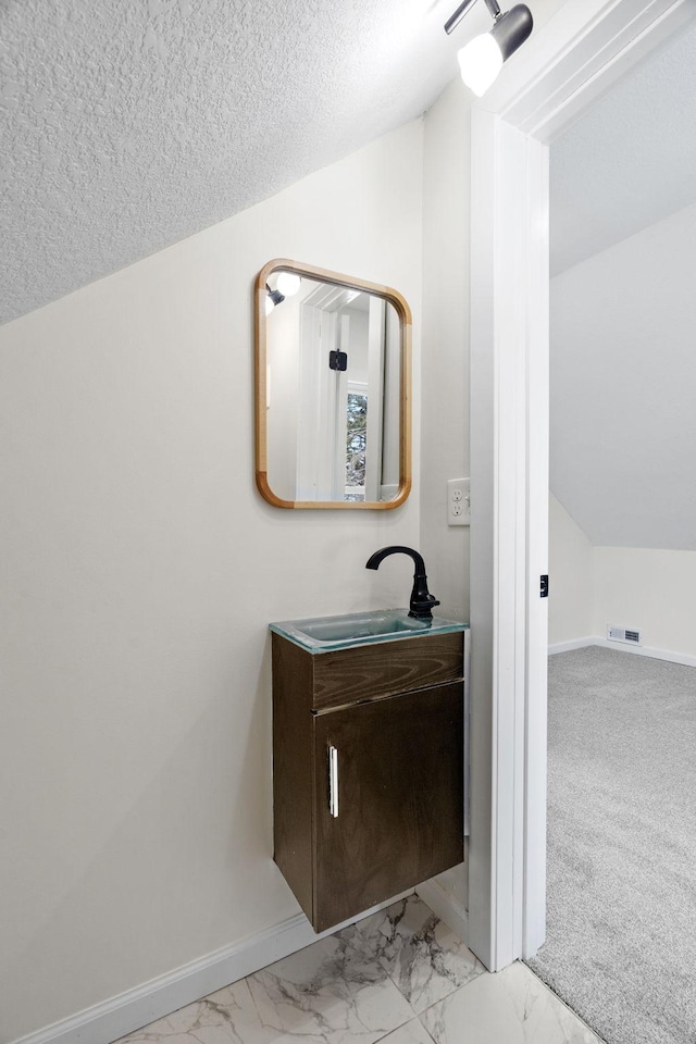 bathroom featuring vanity, vaulted ceiling, and a textured ceiling