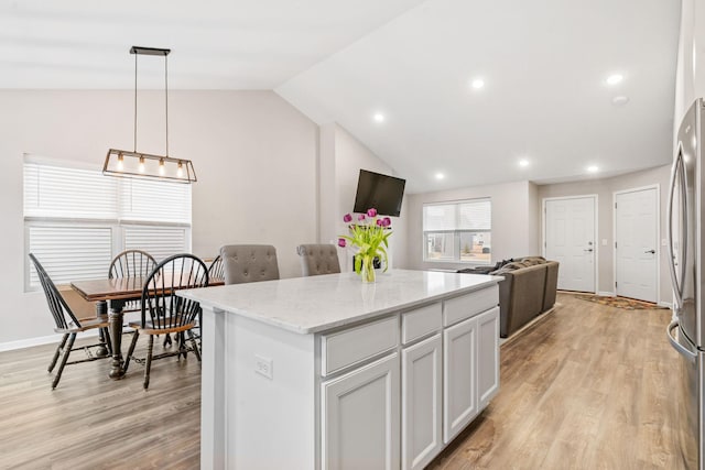 kitchen featuring pendant lighting, a center island, light stone counters, light hardwood / wood-style floors, and vaulted ceiling