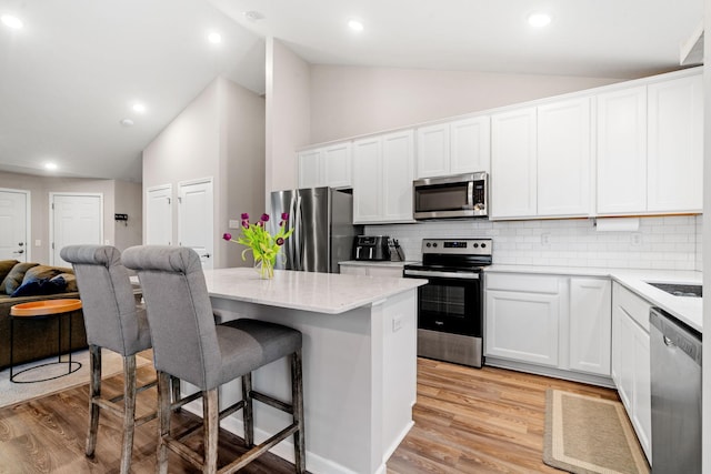 kitchen with a kitchen island, appliances with stainless steel finishes, a breakfast bar area, white cabinets, and light hardwood / wood-style floors