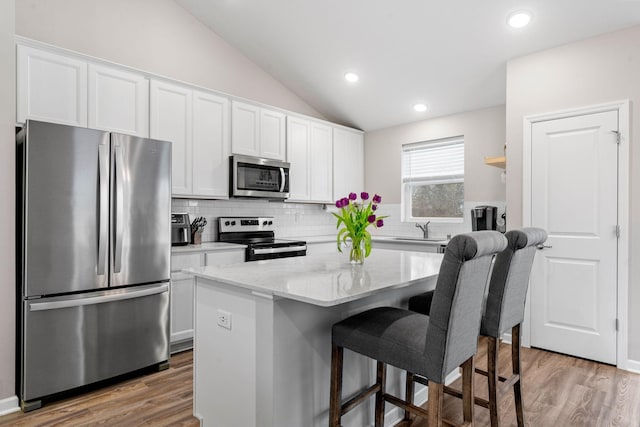 kitchen with a kitchen island, a breakfast bar, white cabinets, stainless steel appliances, and light stone countertops