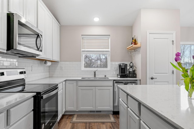 kitchen with sink, appliances with stainless steel finishes, white cabinetry, tasteful backsplash, and light stone countertops