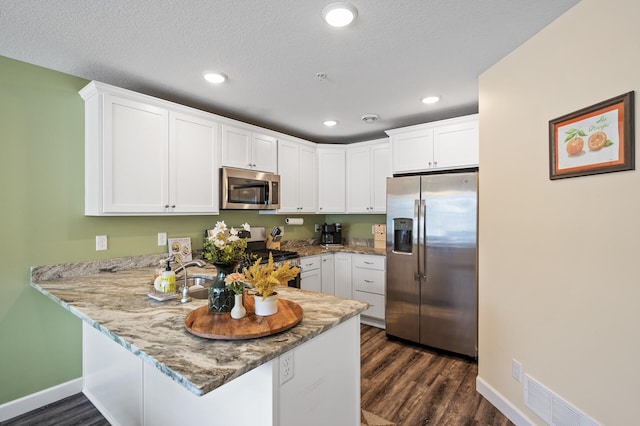 kitchen featuring dark wood-type flooring, appliances with stainless steel finishes, kitchen peninsula, and white cabinets