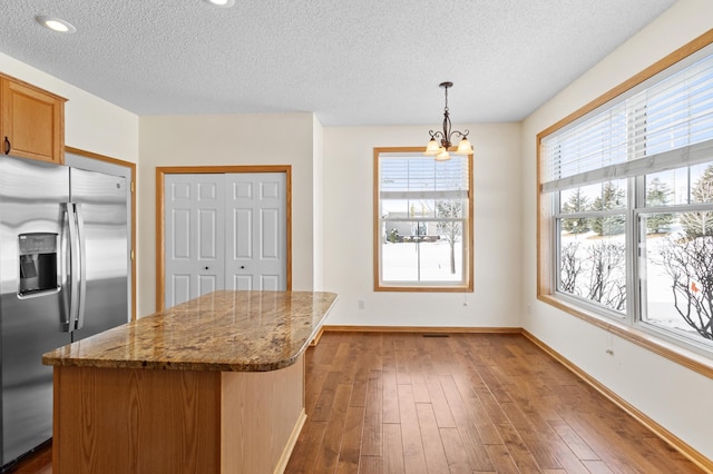 kitchen featuring stainless steel refrigerator with ice dispenser, light stone counters, hanging light fixtures, a textured ceiling, and dark hardwood / wood-style floors