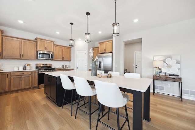 kitchen with a kitchen island, a breakfast bar area, light wood-type flooring, light countertops, and appliances with stainless steel finishes