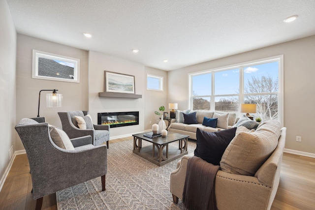 living room with baseboards, recessed lighting, a glass covered fireplace, and wood finished floors