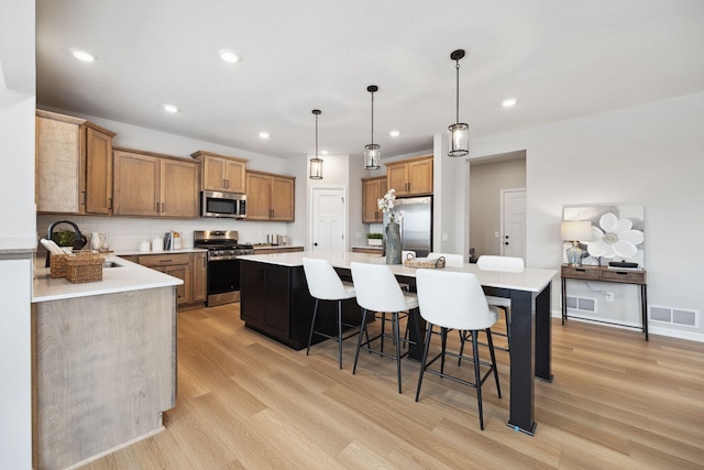 kitchen with appliances with stainless steel finishes, a sink, light wood-style flooring, a kitchen island, and visible vents