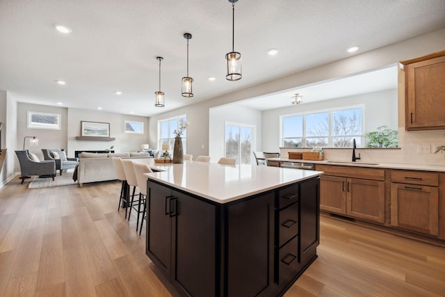 kitchen featuring brown cabinets, a sink, light wood-style floors, light countertops, and open floor plan