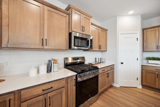 kitchen with brown cabinetry, backsplash, light wood-type flooring, light countertops, and stainless steel appliances