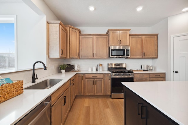 kitchen featuring a sink, light countertops, stainless steel appliances, light wood-type flooring, and backsplash
