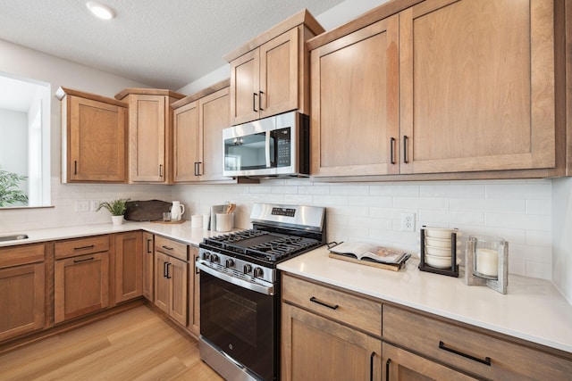 kitchen with decorative backsplash, a textured ceiling, light countertops, light wood-style floors, and stainless steel appliances
