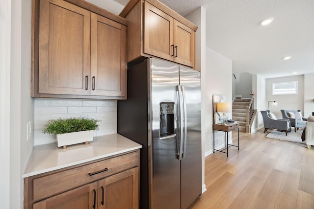 kitchen featuring light countertops, open floor plan, decorative backsplash, light wood-type flooring, and stainless steel refrigerator with ice dispenser
