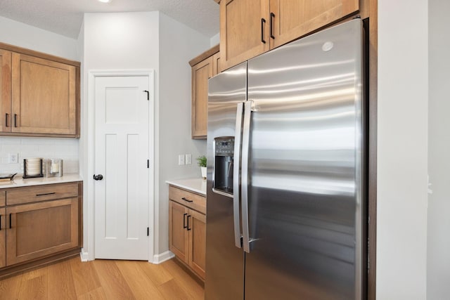 kitchen featuring stainless steel fridge, light wood finished floors, light countertops, brown cabinetry, and backsplash