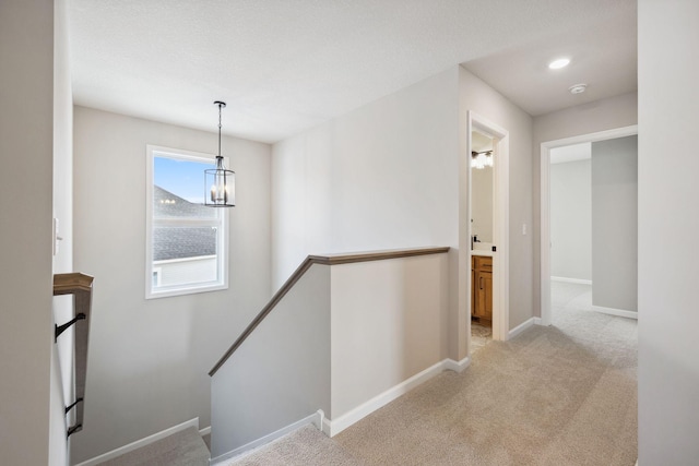 hallway featuring light colored carpet, baseboards, a notable chandelier, and an upstairs landing
