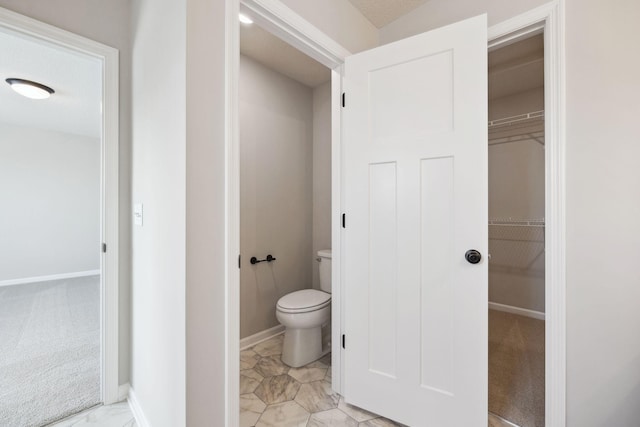 bathroom featuring baseboards, a walk in closet, and toilet