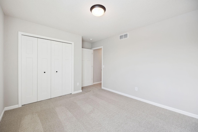 unfurnished bedroom with visible vents, baseboards, a closet, and light carpet
