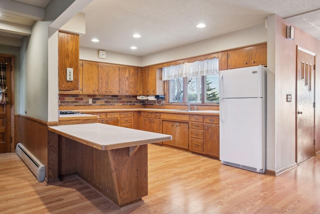 kitchen featuring a breakfast bar area, light hardwood / wood-style flooring, kitchen peninsula, white fridge, and a baseboard heating unit