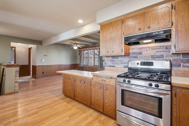 kitchen with light hardwood / wood-style flooring, ceiling fan, stainless steel range with gas stovetop, tasteful backsplash, and beamed ceiling