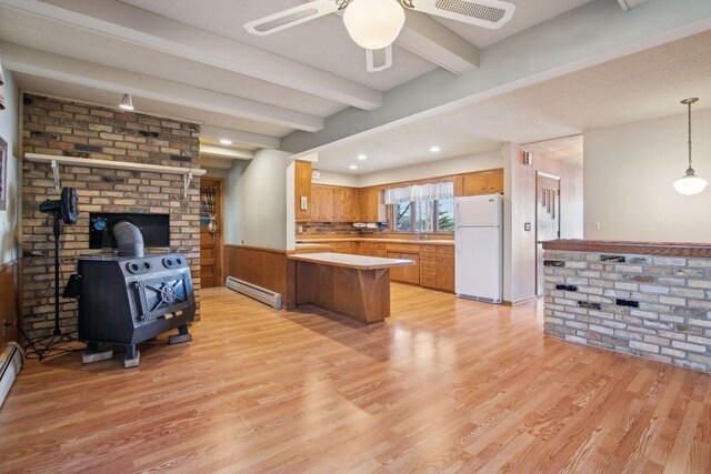 kitchen featuring a wood stove, white refrigerator, a baseboard heating unit, kitchen peninsula, and beam ceiling