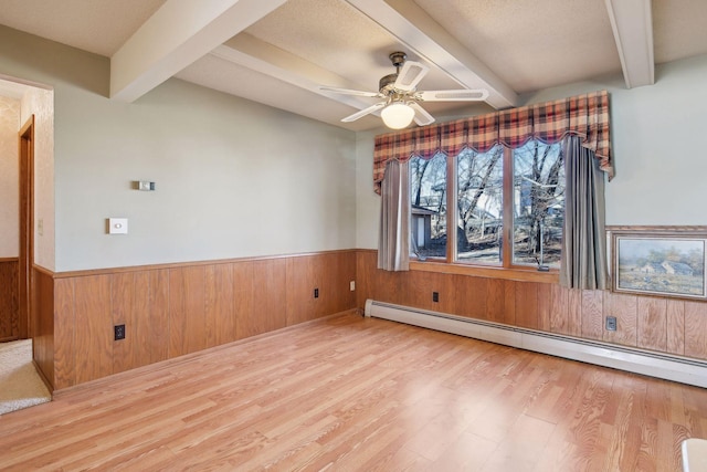 interior space featuring wood walls, beamed ceiling, a baseboard radiator, ceiling fan, and light hardwood / wood-style flooring