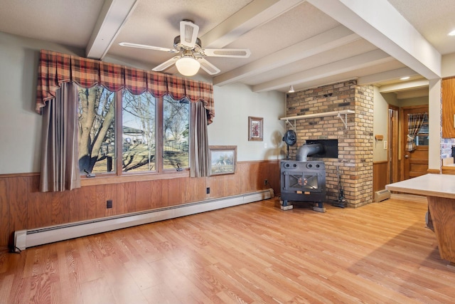 living room with beam ceiling, light wood-type flooring, a wood stove, and baseboard heating