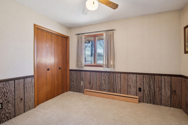 carpeted bedroom with ceiling fan, wood walls, baseboard heating, and a closet